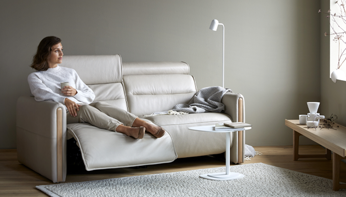 Stressless Sofa • Eine Frau sitzt auf einem cremefarbenen Ledersofa und schaut aus dem Fenster. Die Fußstütze des Sofas ist ausgefahren • Meyerhoff