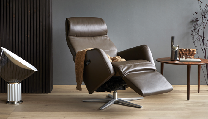 Stressless Sessel • Brauner Sessel mit ausgefahrener Fußstütze, daneben ein Beistelltisch mit Dekoration • Meyerhoff Stressless Sessel • Brauner Sessel mit ausgefahrener Fußstütze, daneben ein Beistelltisch mit Dekoration • Meyerhoff