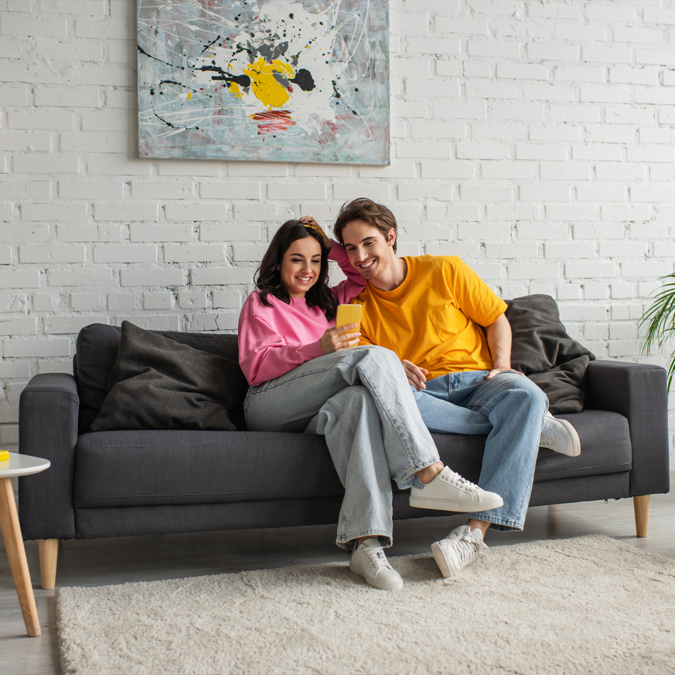 WhatsApp Premium • Paar sitzt auf dem Sofa und schaut gemeinsam aufs Handy • Meyerhoff